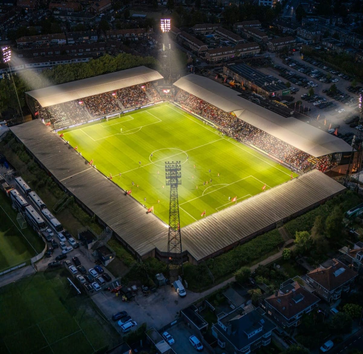 A floodlit football stadium during an evening match, seen from the air